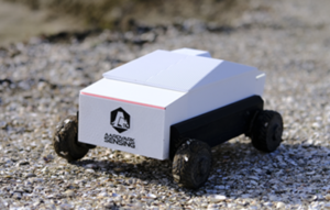 white autonomous robot driving across pathway of pebbles and shells